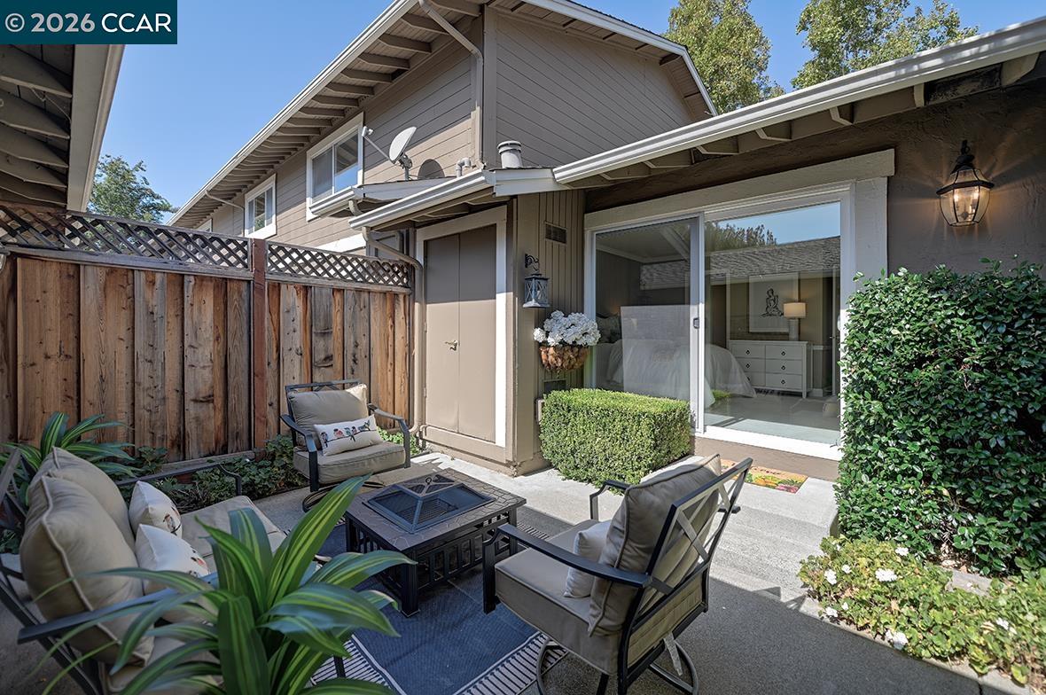 Furnished patio with cushioned seating beside a sliding glass door and fenced courtyard.