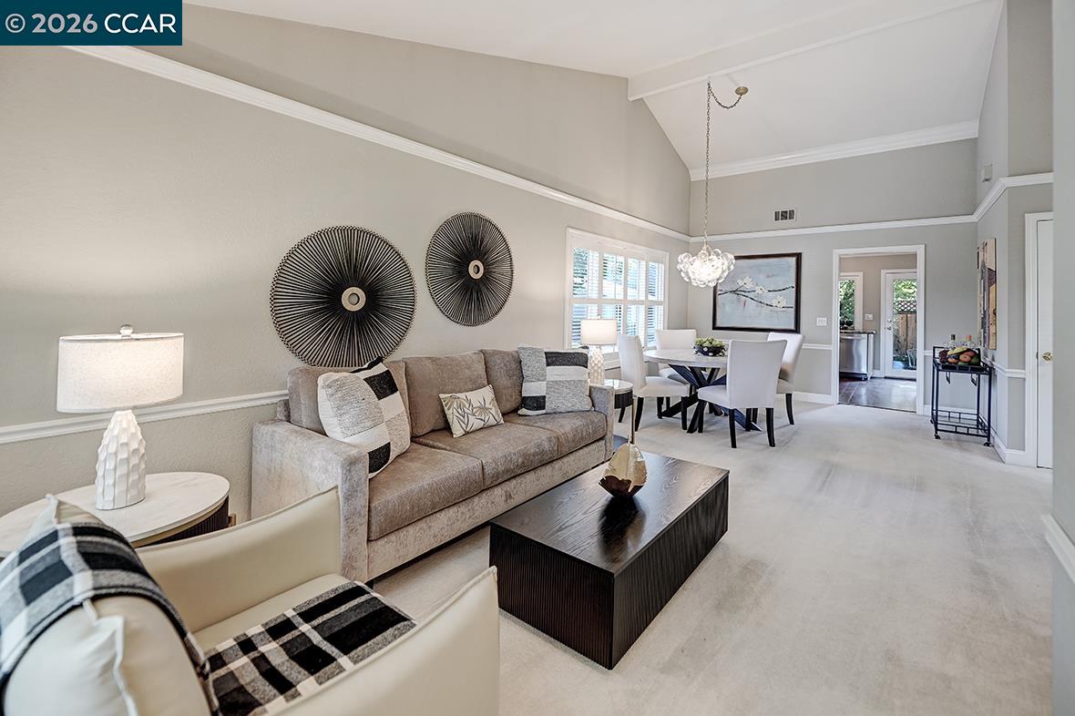 Open-plan living and dining room with a vaulted ceiling, neutral furnishings, and a chandelier.