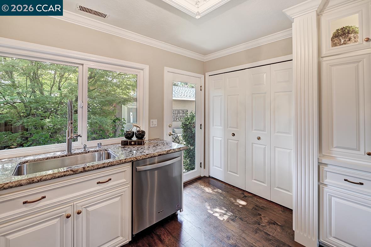 Kitchen with white cabinetry, granite counters, and a wide window overlooking trees.