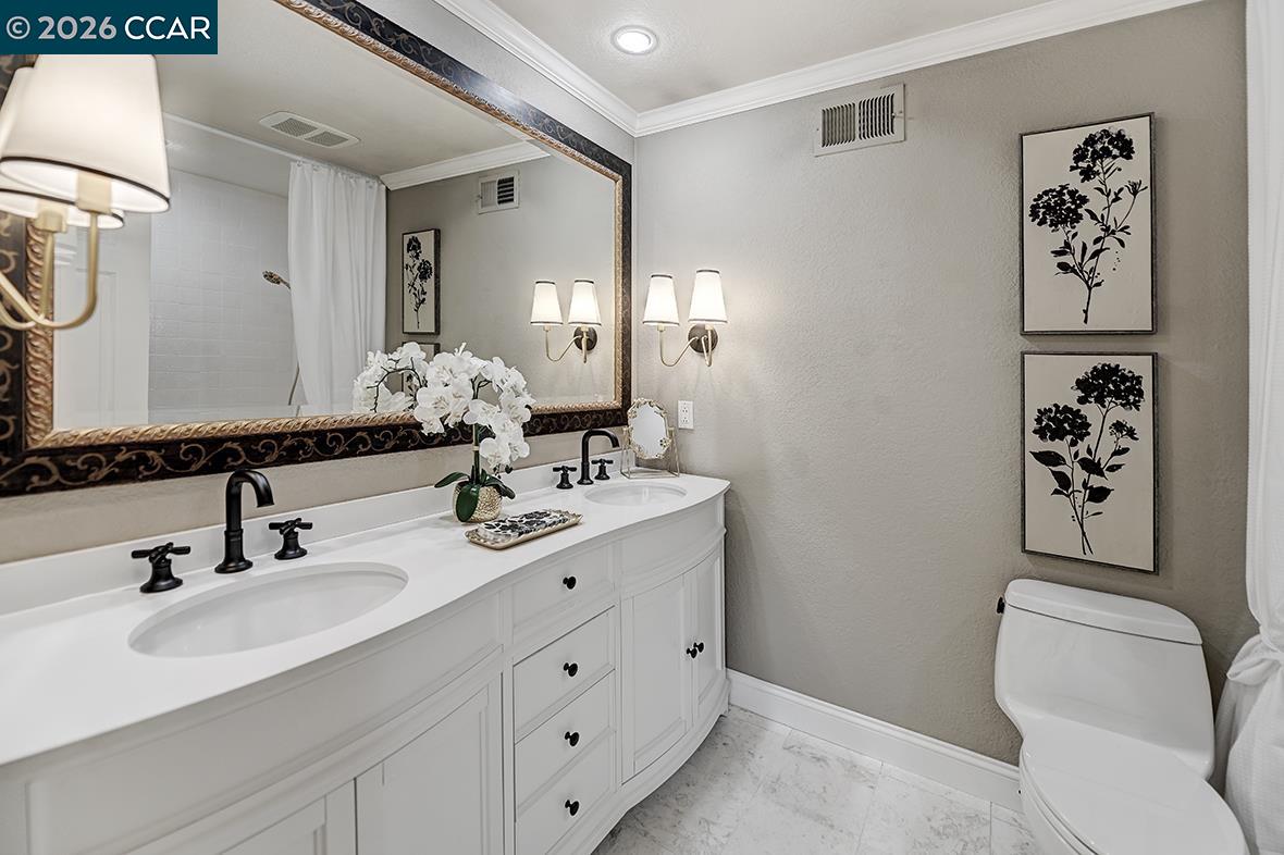 Bathroom with a white double-sink vanity, ornate mirror, and botanical wall art.