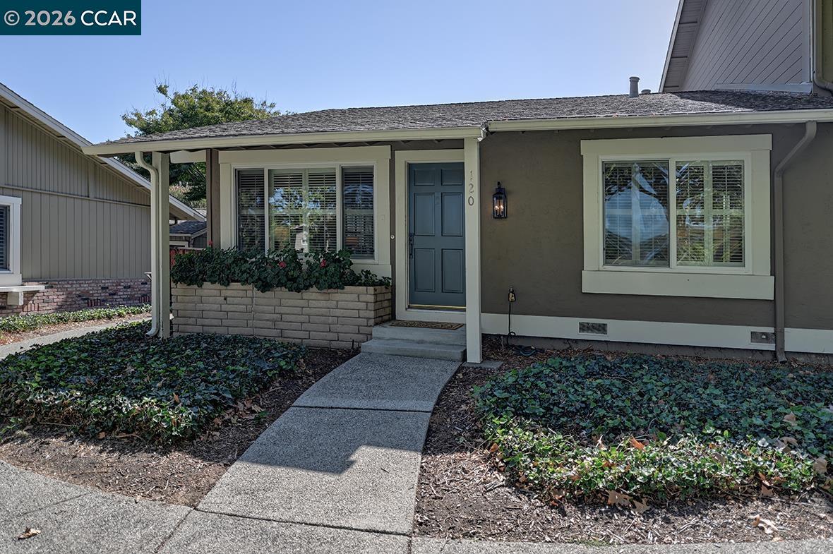 Single-story home with a blue-green front door, covered entry, and walkway through planted beds.