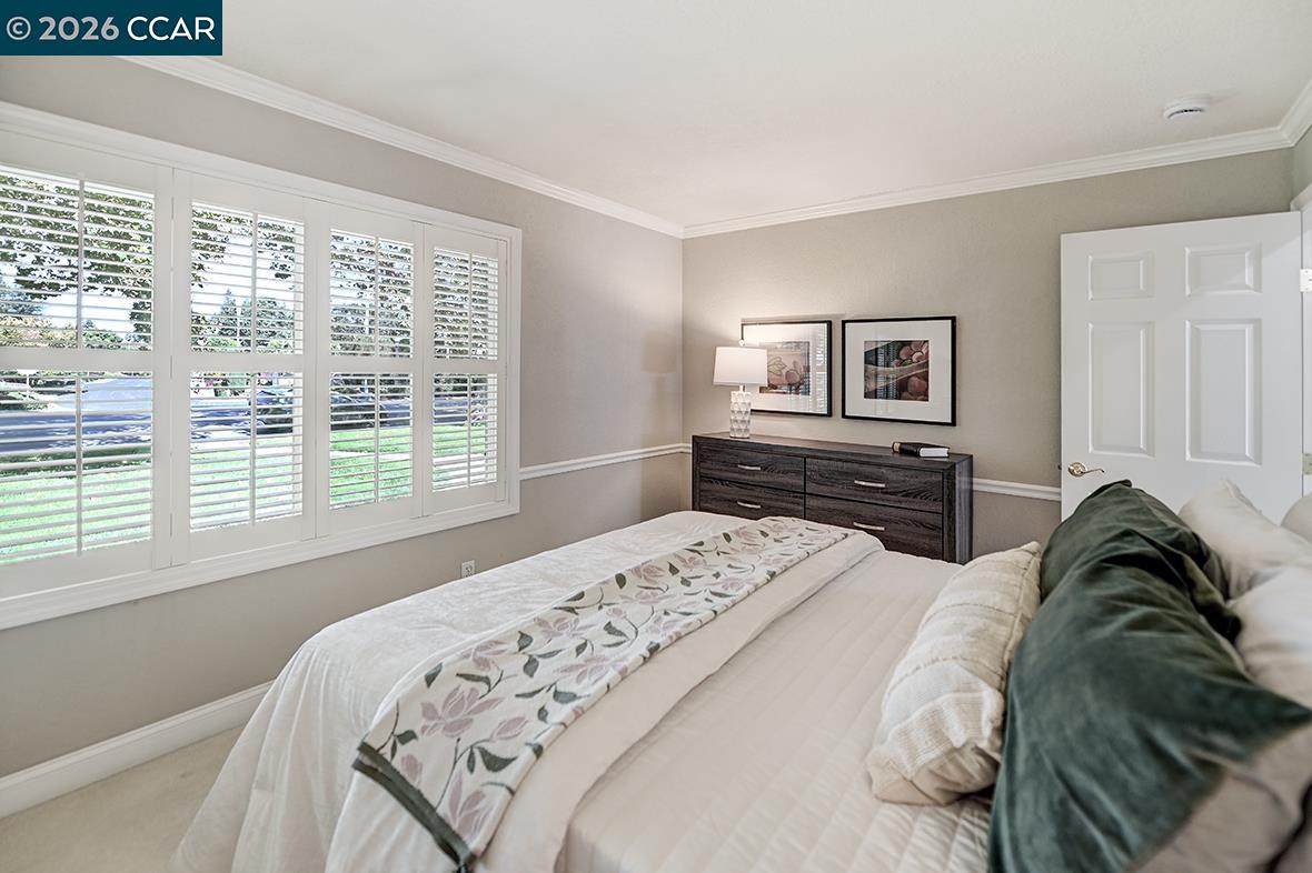 Bedroom with plantation shutters, a floral bed runner, and a dark dresser beneath framed artwork.