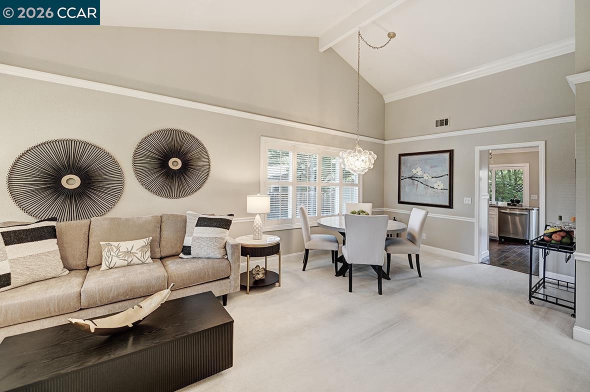 Living and dining room with a beige sofa, round table, shuttered windows, and vaulted ceiling.