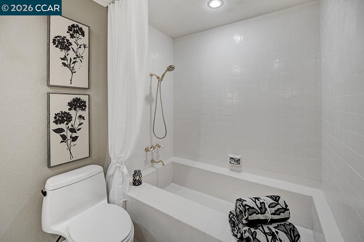Bathroom with a white tiled bathtub and shower, tied-back curtain, and framed botanical prints.