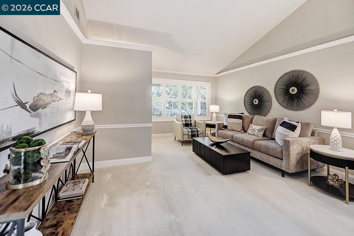 Staged living room with a beige sectional, black coffee table, and vaulted tray ceiling.