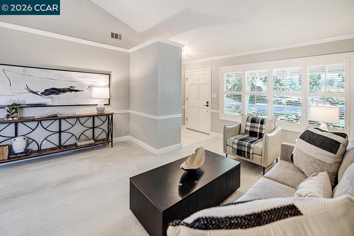 Furnished living room with plantation-shuttered windows, light carpet, and a black coffee table.