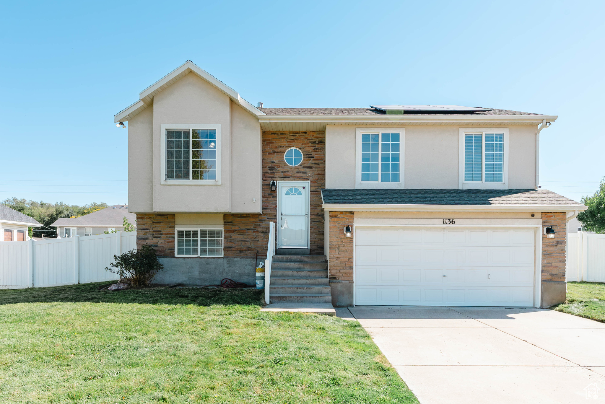 Two-story house with stone accents, solar panels, a double garage, and front lawn.