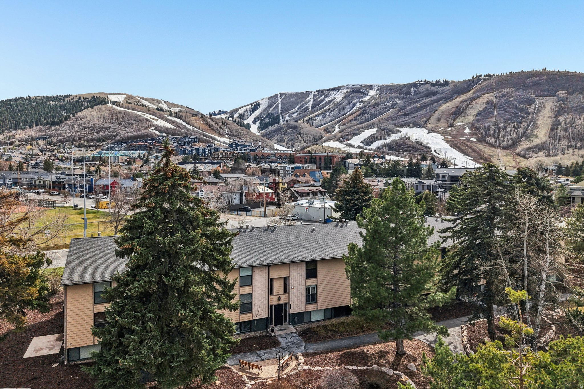 Tan residential building among evergreens, with Park City ski slopes in the background.
