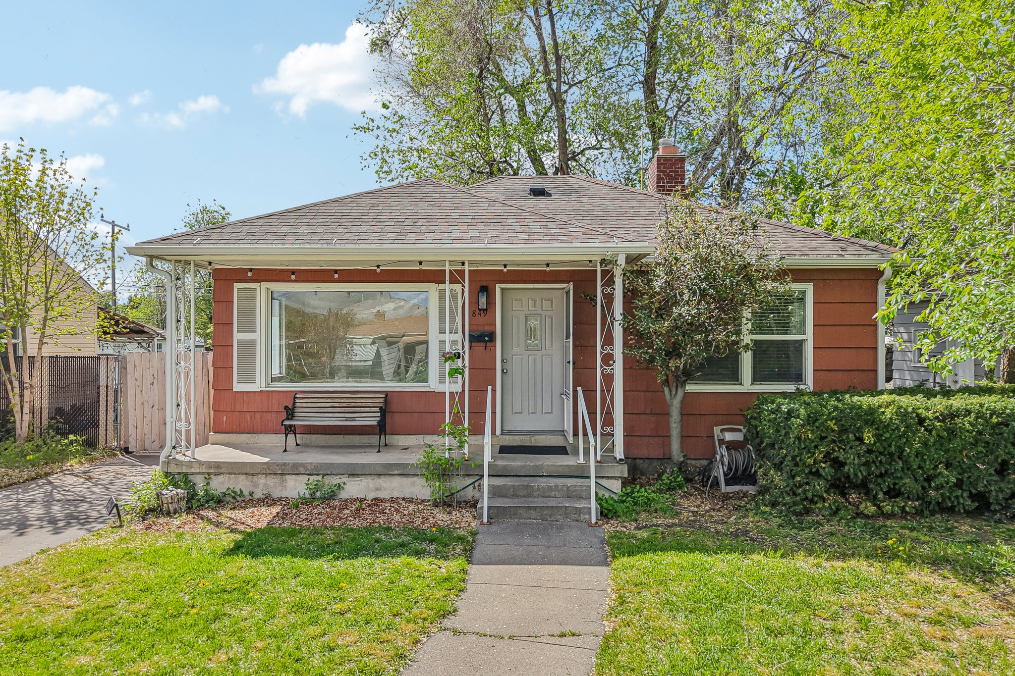Red-sided single-story home with a covered porch, front bench, and walkway through the lawn.