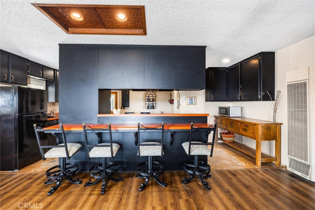 Kitchen with a large orange-topped breakfast bar, four metal stools, and dark cabinetry.