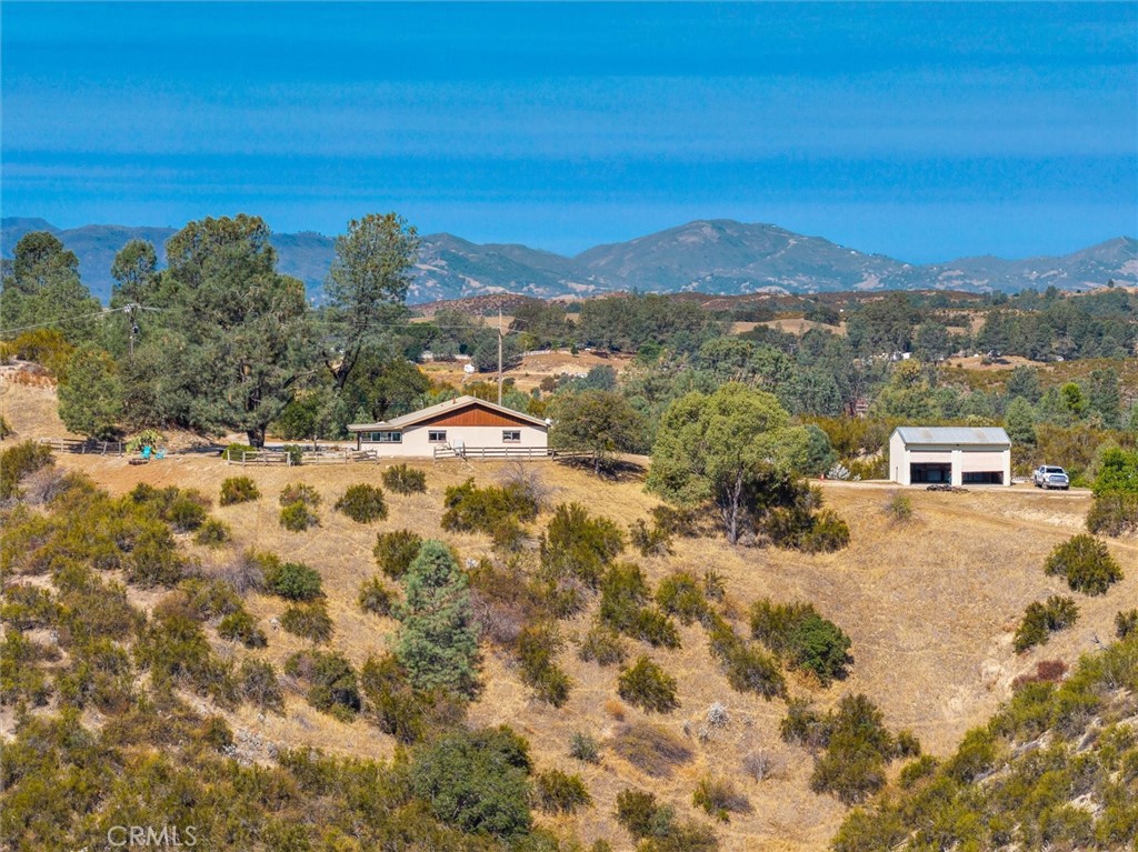 Rural property with a house and detached outbuilding on dry, rolling acreage, backed by distant mountains.
