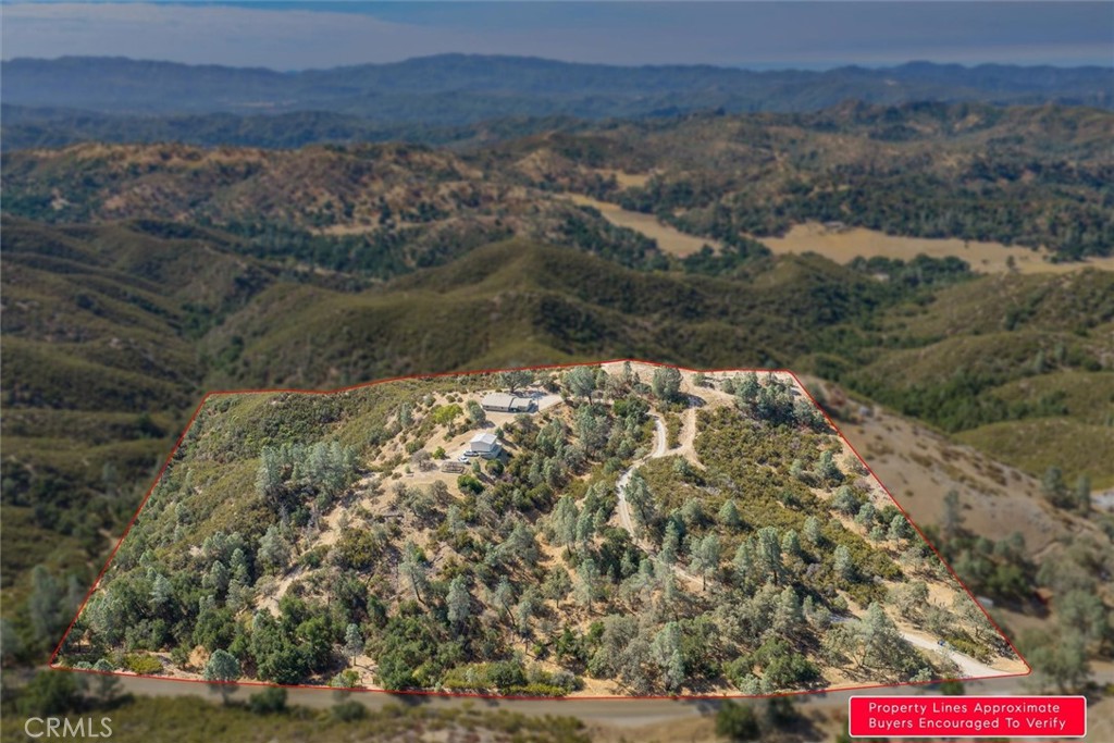 Aerial view of a hillside parcel outlined in red, with scattered trees, a few buildings, and winding dirt roads.