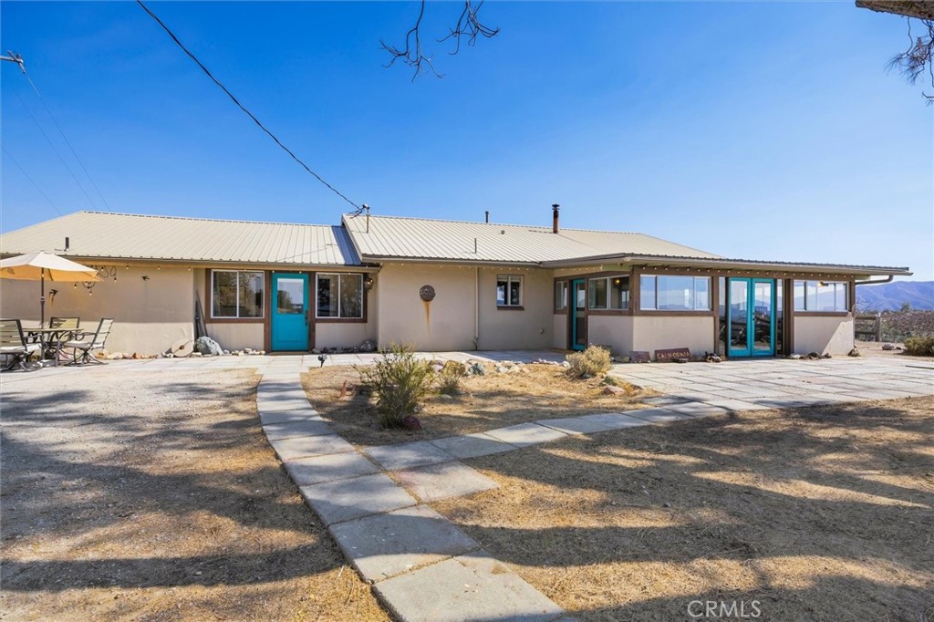Single-story home with a light metal roof, turquoise doors, and a concrete walkway across the dry yard.