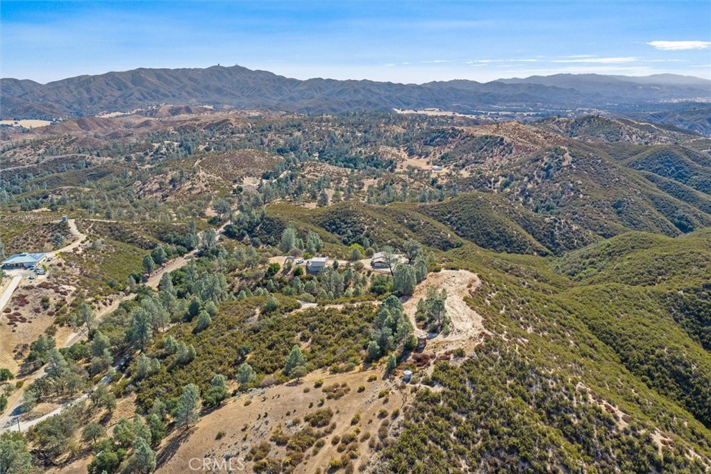 Aerial view of a rural property amid rolling hills, with scattered buildings and distant mountain ranges.