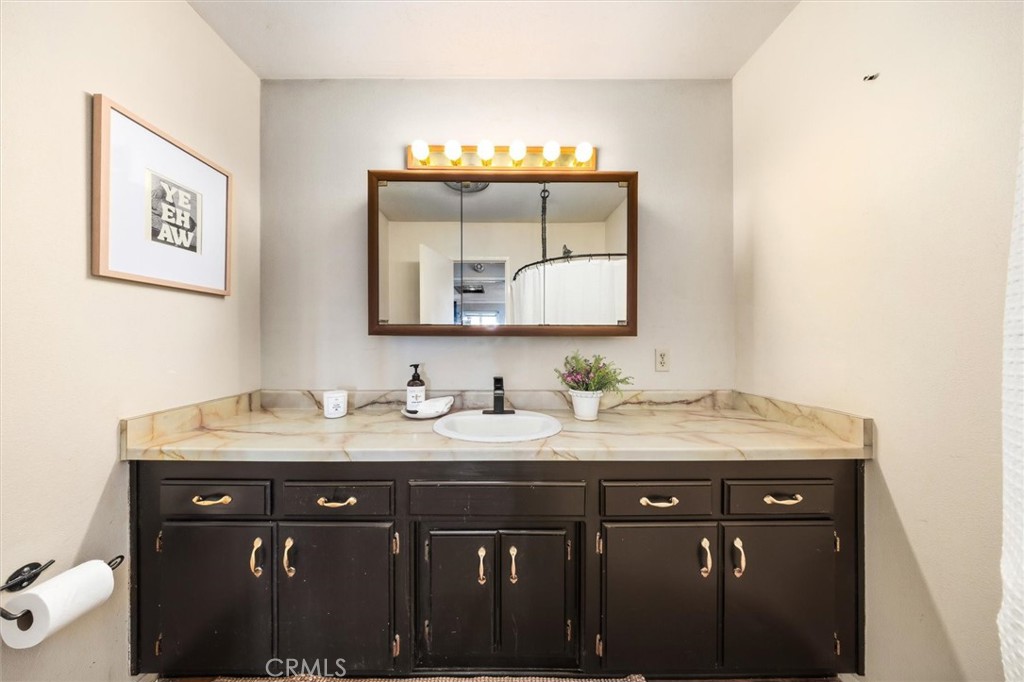 Bathroom vanity with dark cabinets, marble-look counter, brass pulls, and a wood-framed mirror.