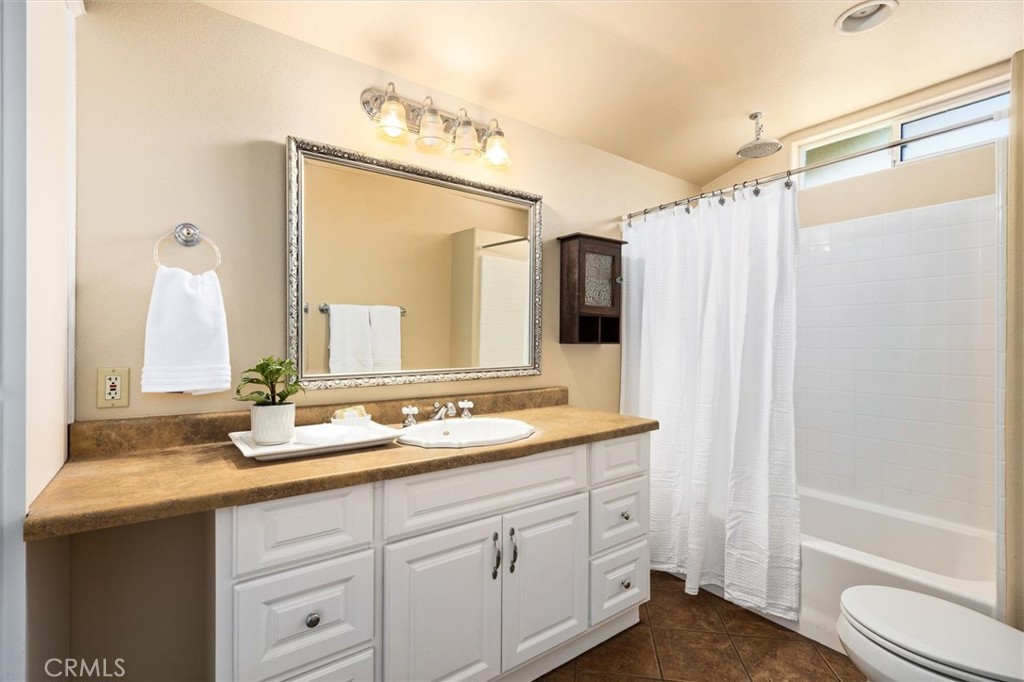 Bathroom with a white vanity, brown countertop, ornate framed mirror, and curtained tub-shower.