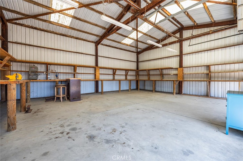 Spacious metal workshop with exposed wooden trusses, concrete floor, and a workbench along the wall.