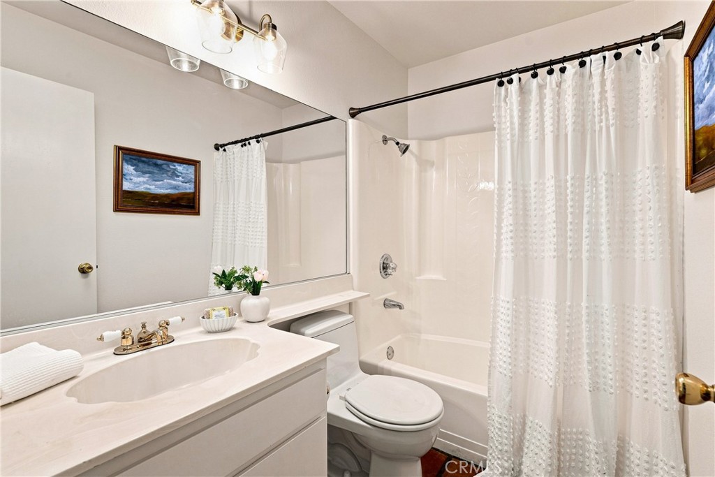 Bathroom with a white vanity, large mirror, and bathtub behind a textured white shower curtain.