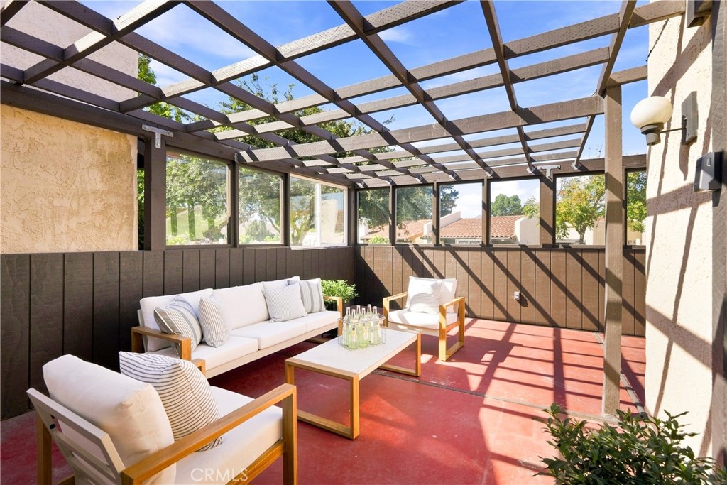 Covered patio with white cushioned seating, red flooring, and a timber pergola overhead.