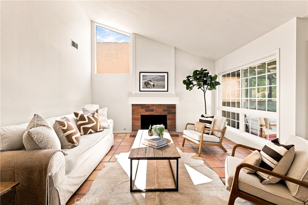 Living room with a brick fireplace, terracotta tile floor, and large windows.