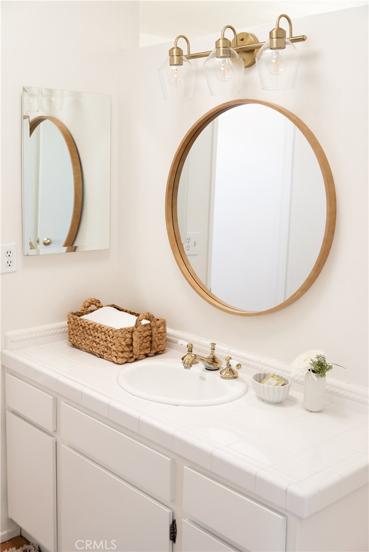 Bathroom vanity with oval wood-framed mirror, brass lights, and white tile countertop.