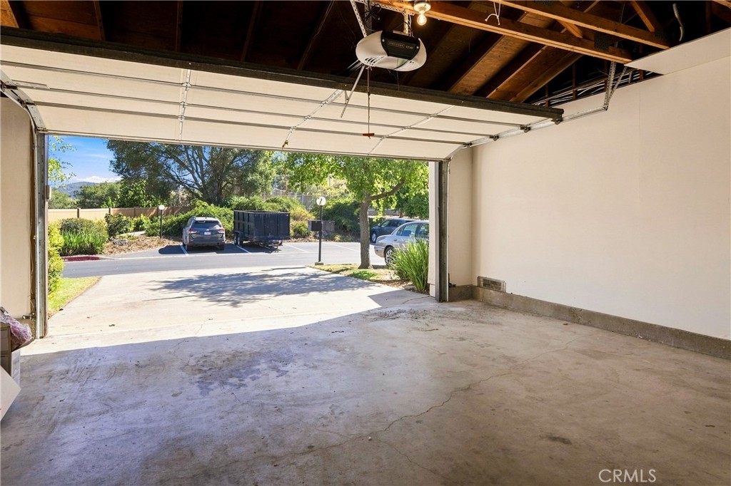Vacant garage with exposed rafters and an open door overlooking the driveway.