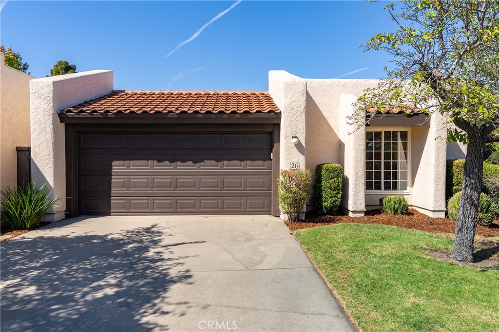 Stucco home with a dark double garage door, tiled roof, and tree-shaded driveway.