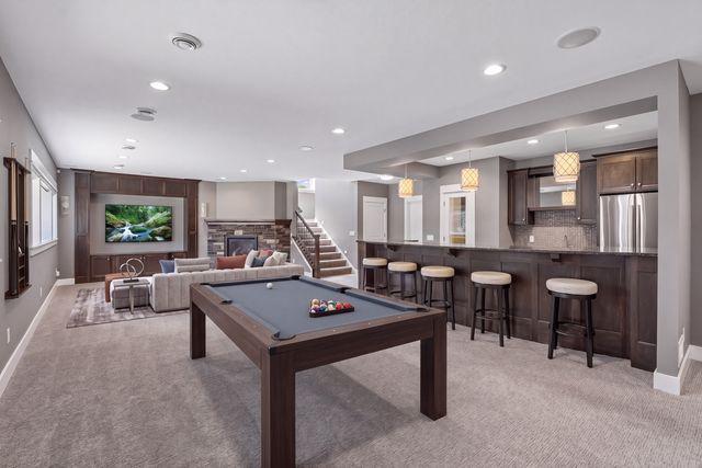 Finished basement recreation room with a pool table, sectional seating, and a long bar with stools.