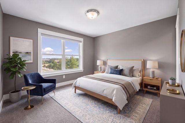Staged bedroom with a large window, navy armchair, and pale patterned rug.