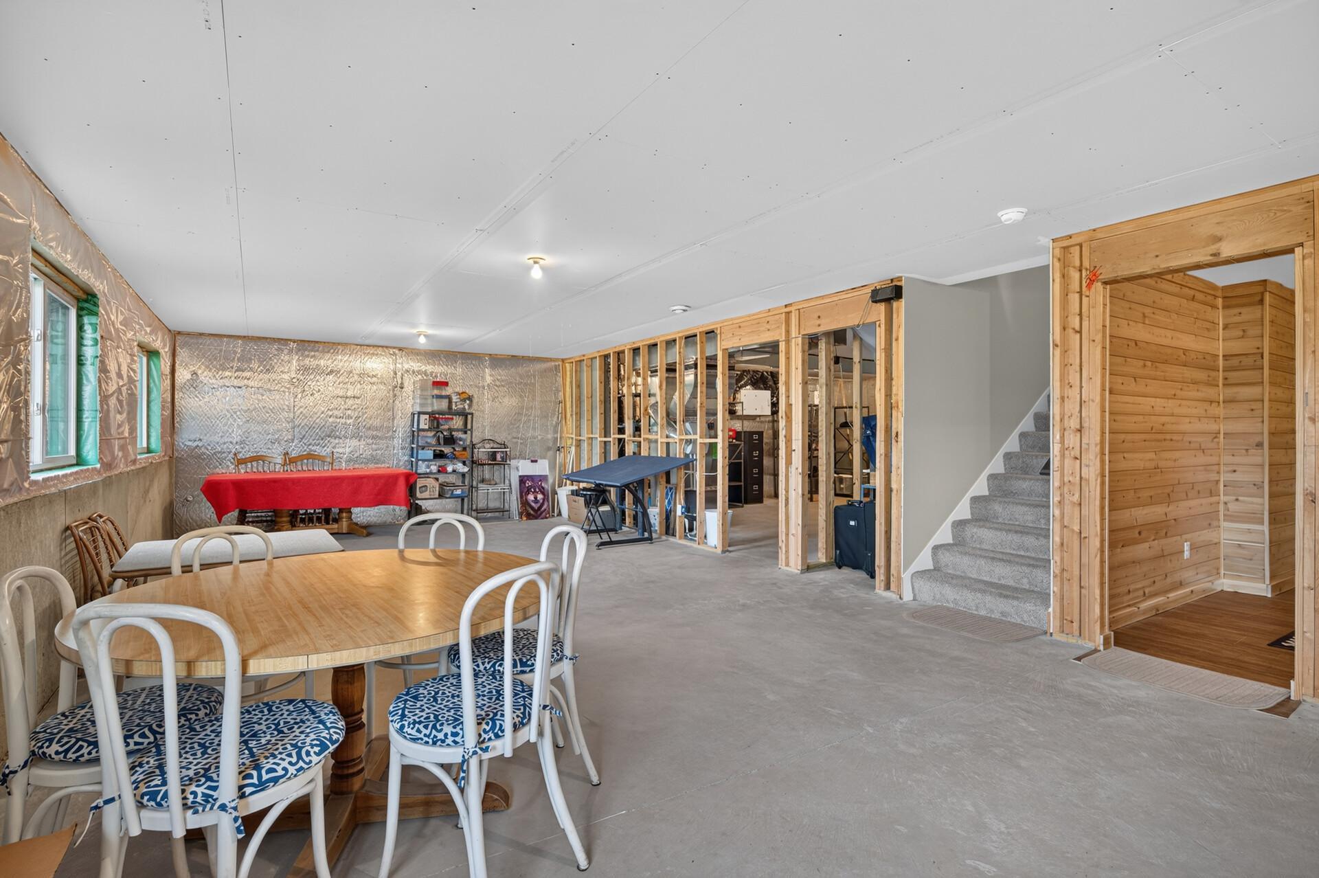Basement with a dining table, exposed framing, carpeted stairs, and a wood-paneled room.