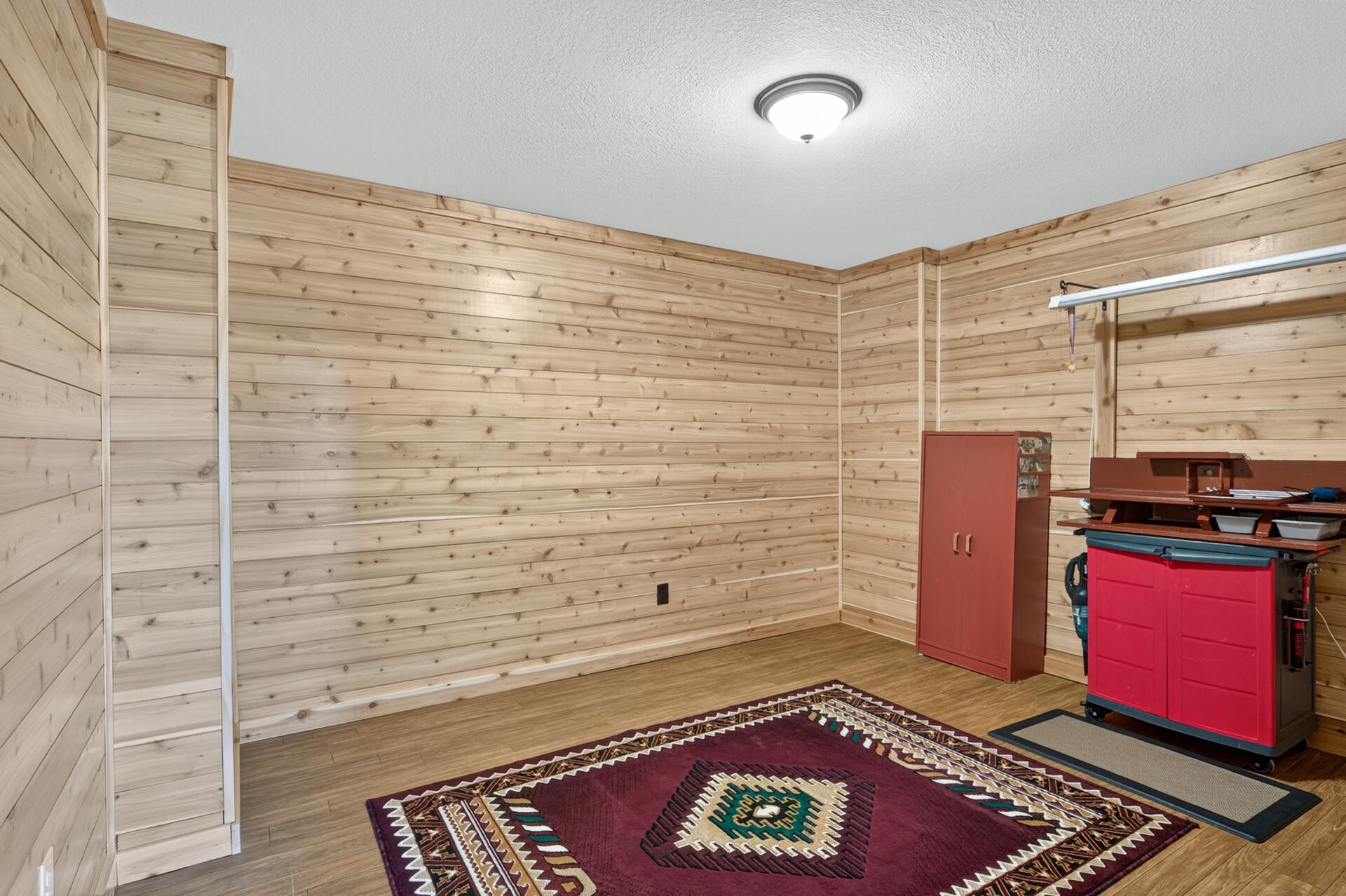 Wood-paneled workshop with a red workbench, storage cabinet, and patterned rug.