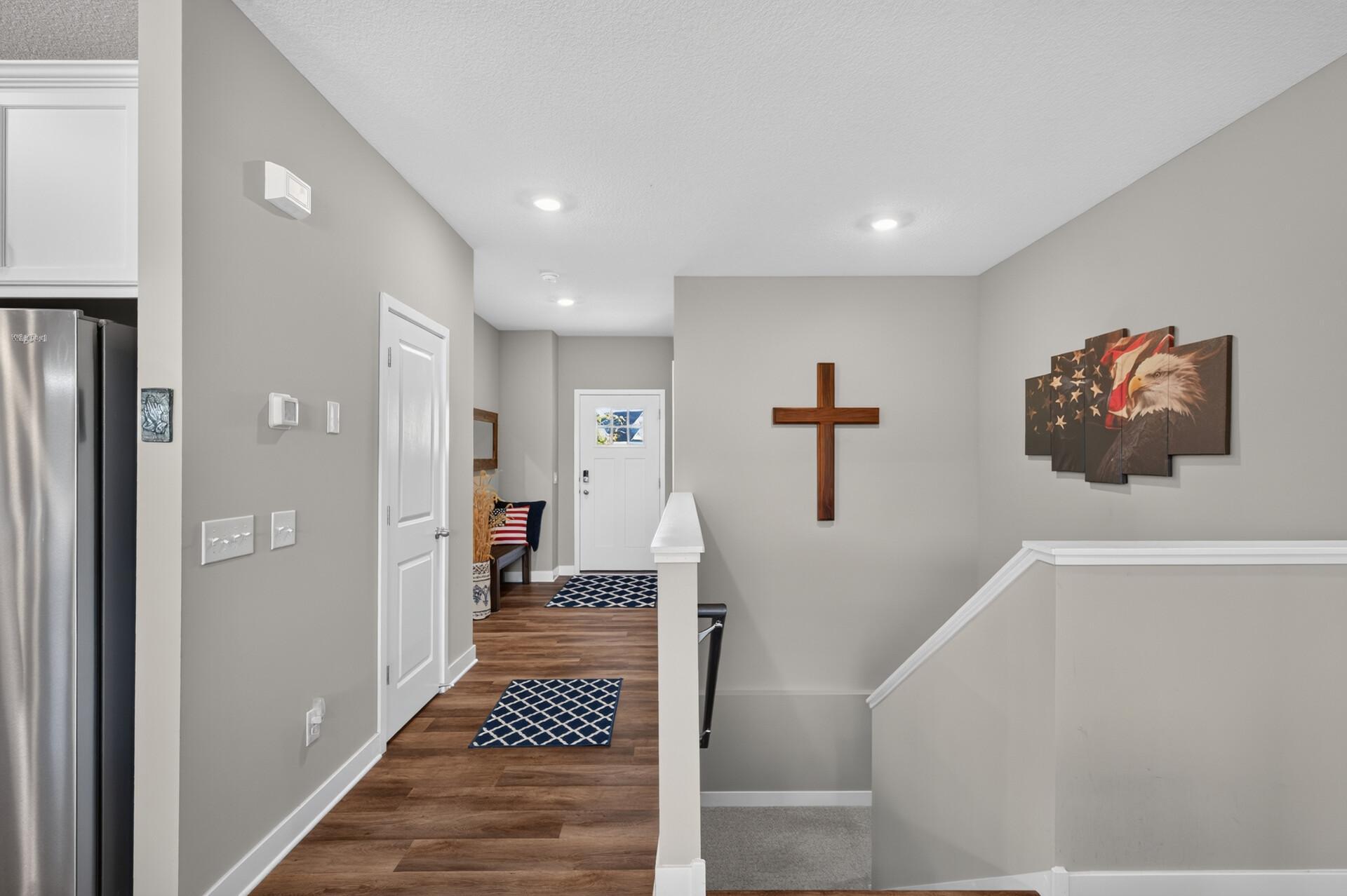 Entry hallway with wood-look flooring, patterned runners, a wall cross, and stairs.