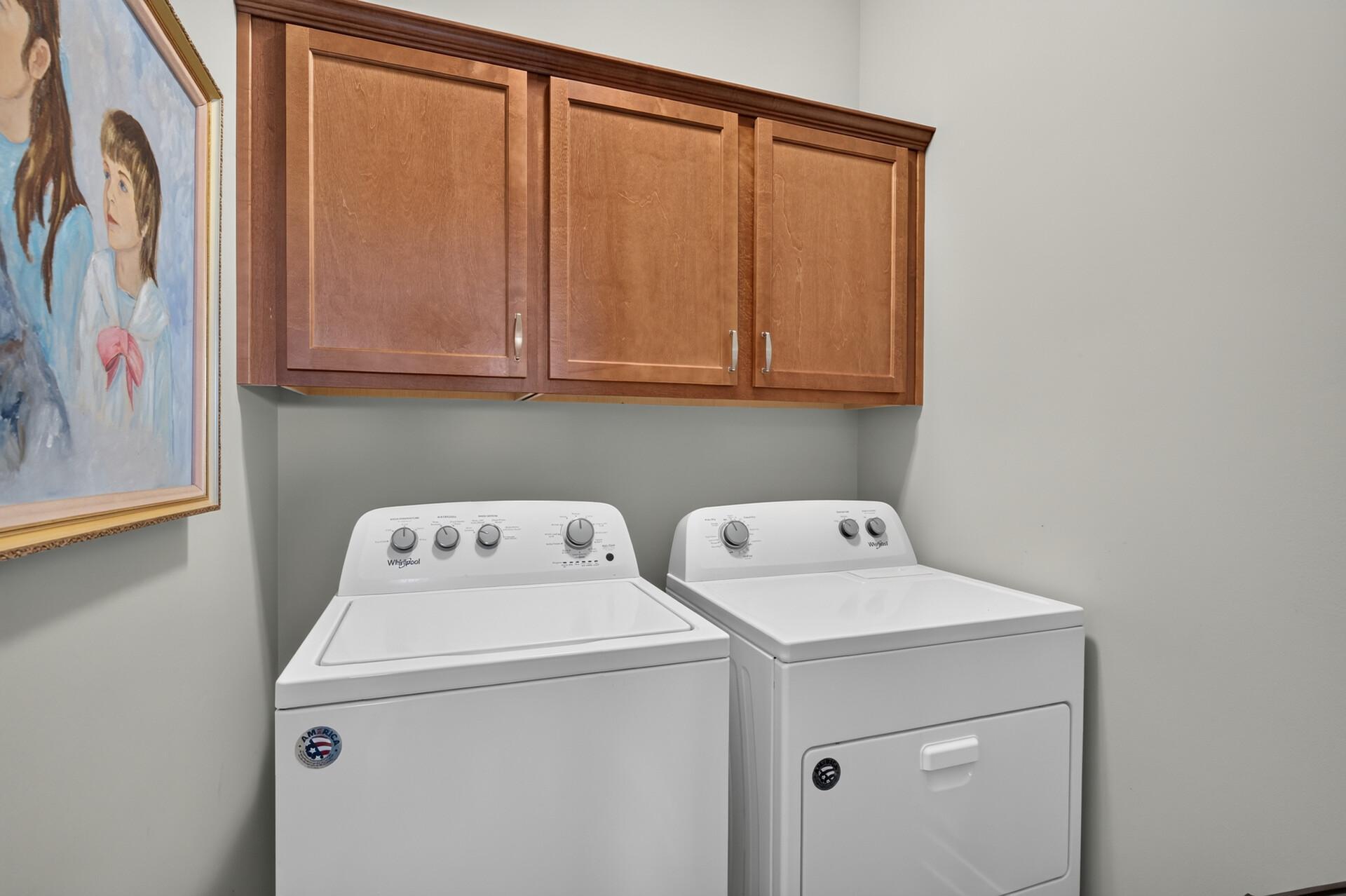 Laundry room with white washer and dryer beneath warm wood cabinets.