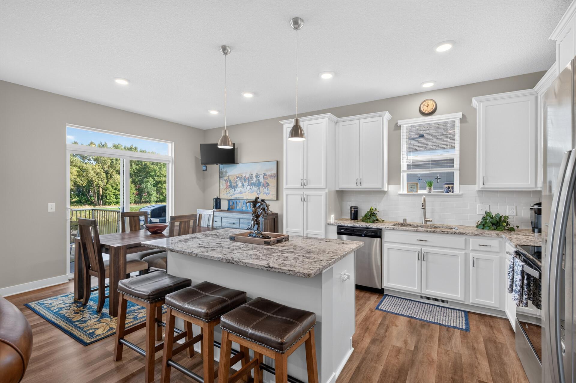Kitchen and dining area with a granite island, white cabinetry, and sliding glass doors.