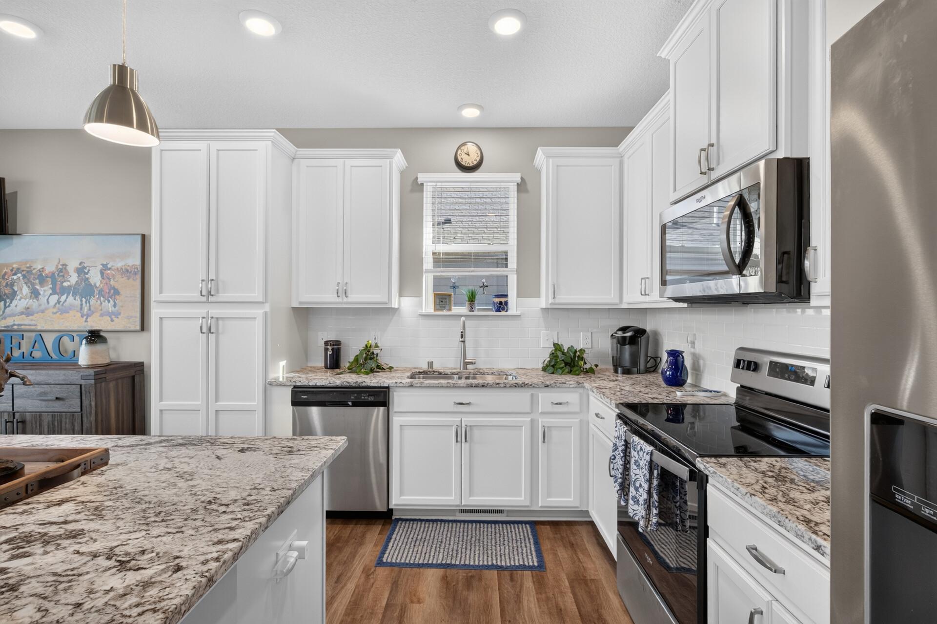 Kitchen with white cabinets, granite counters, stainless steel appliances, and a sink beneath the window.