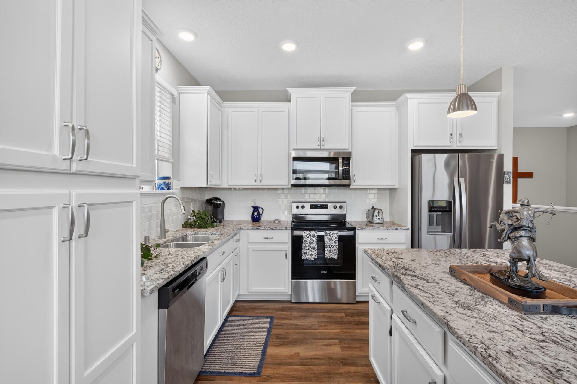 Bright kitchen with white cabinets, granite counters, stainless steel appliances, and a large island.