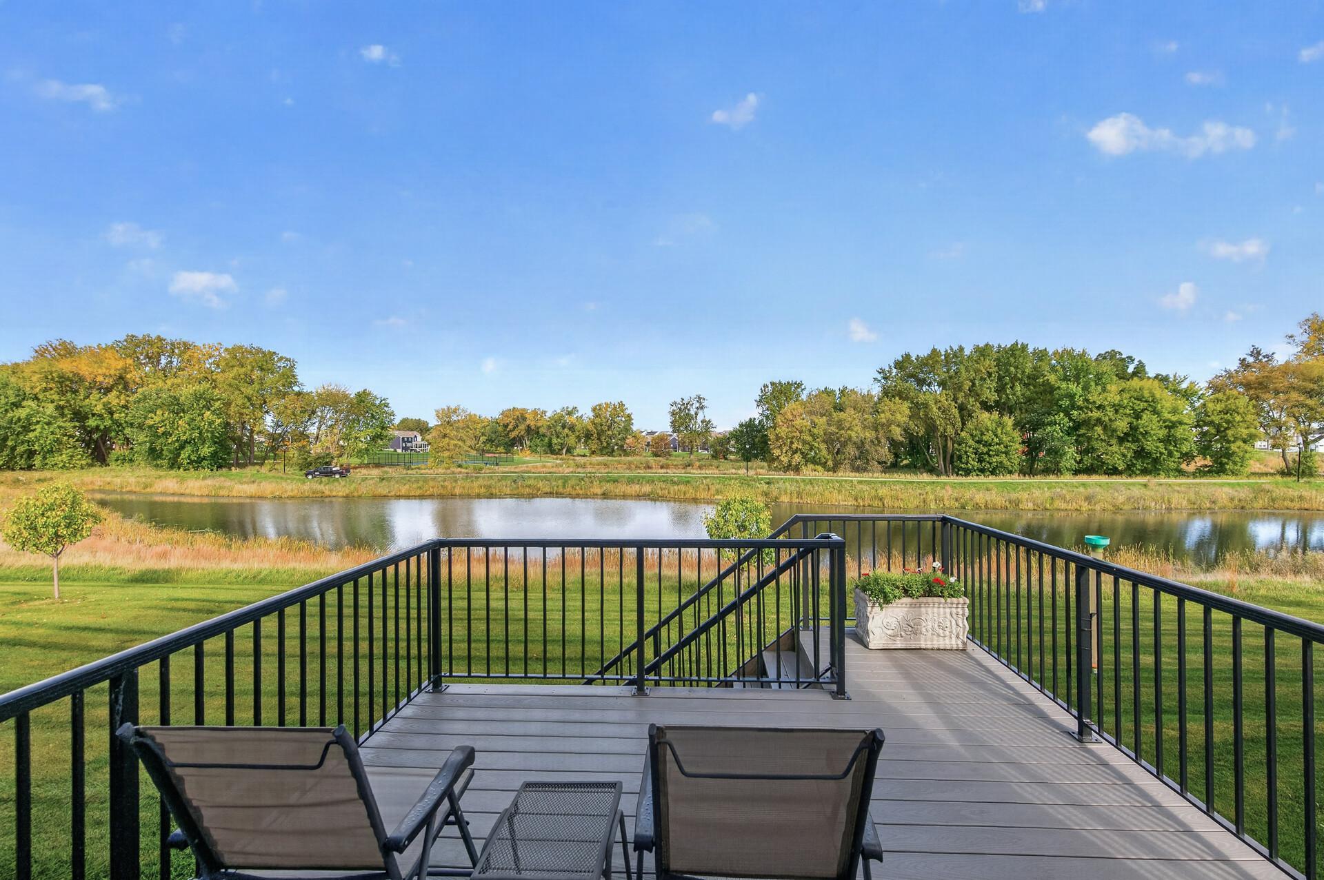 Deck overlooking a pond, with black railings, patio chairs, and autumn trees.