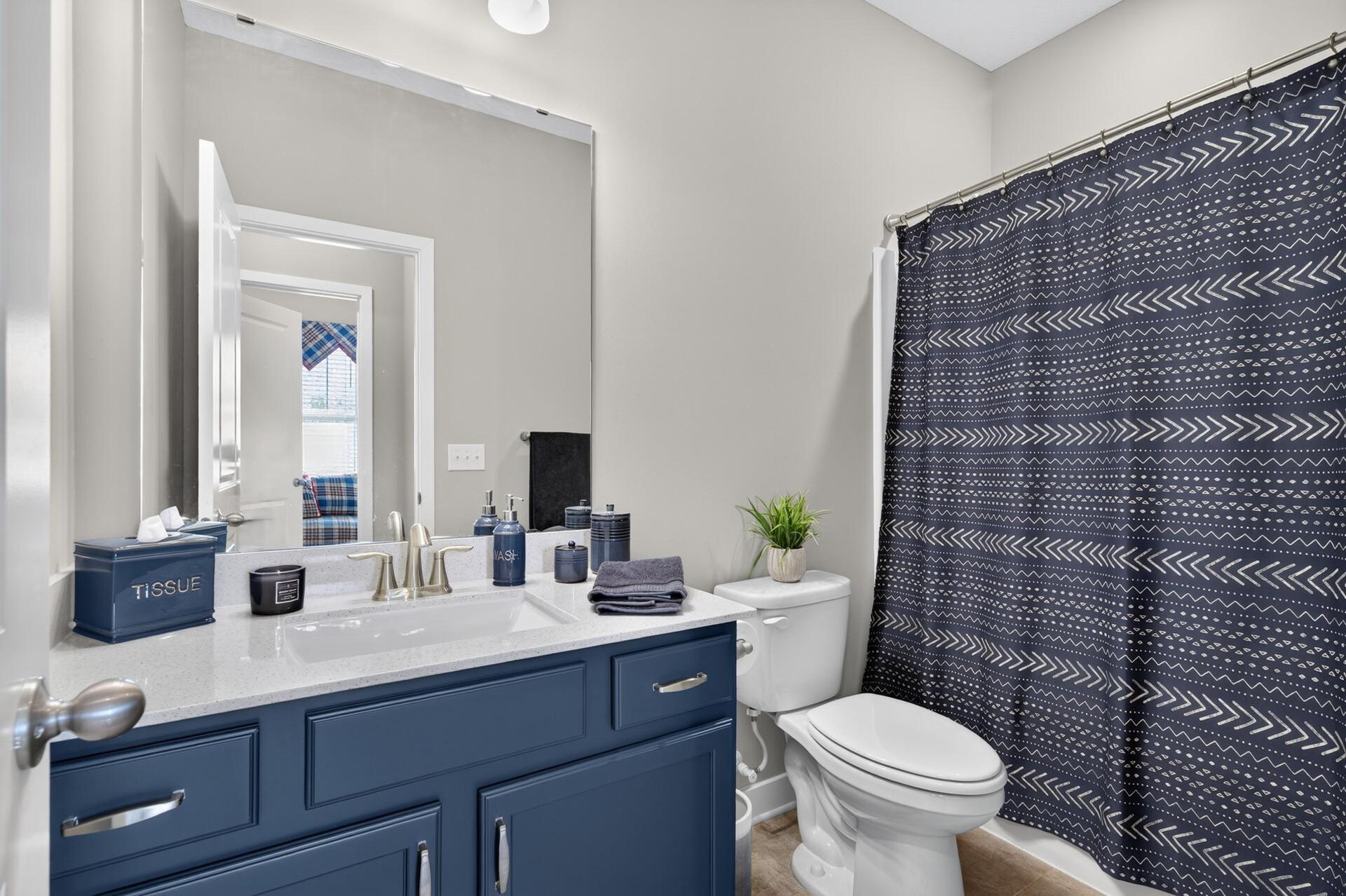 Bathroom with a navy vanity, white countertop, and geometric-patterned shower curtain.