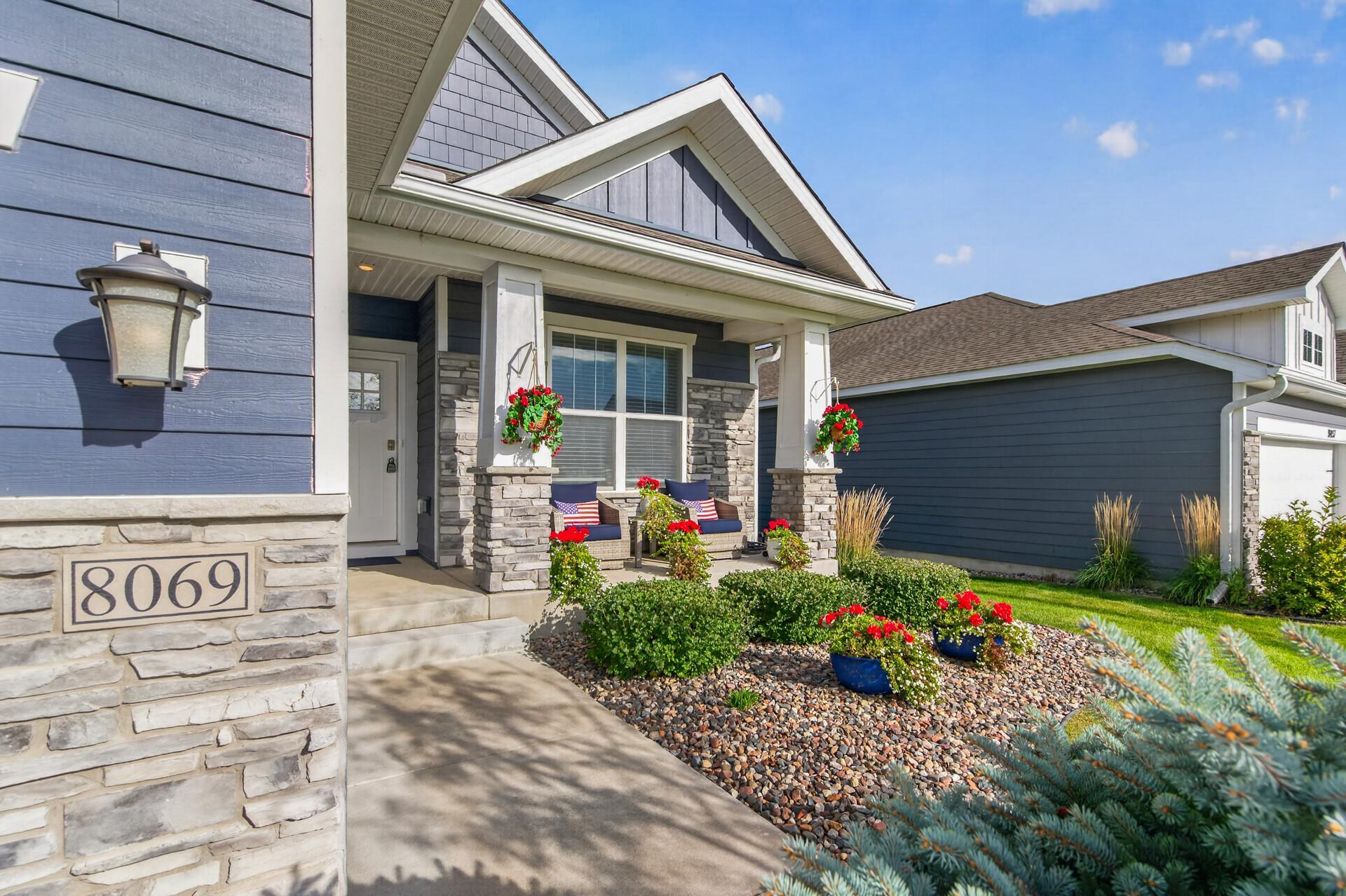 Blue house entrance with a stone porch, flower baskets, and address number 8069.