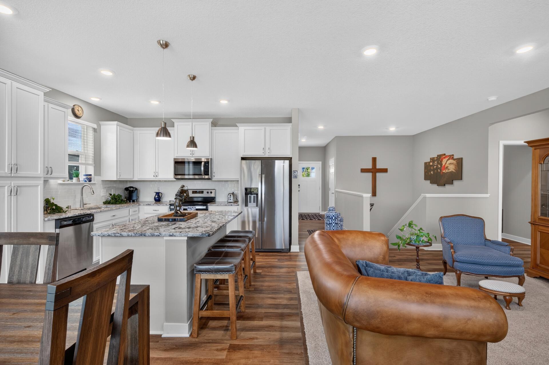 Open-plan kitchen and living area with a granite island, white cabinets, stainless appliances, and leather sofa.