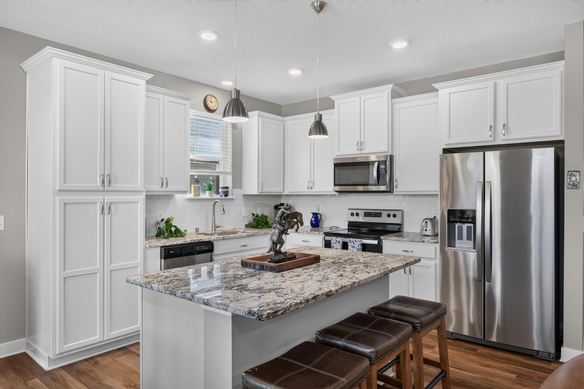 Kitchen with white cabinets, granite island, stainless steel appliances, and dark bar stools.
