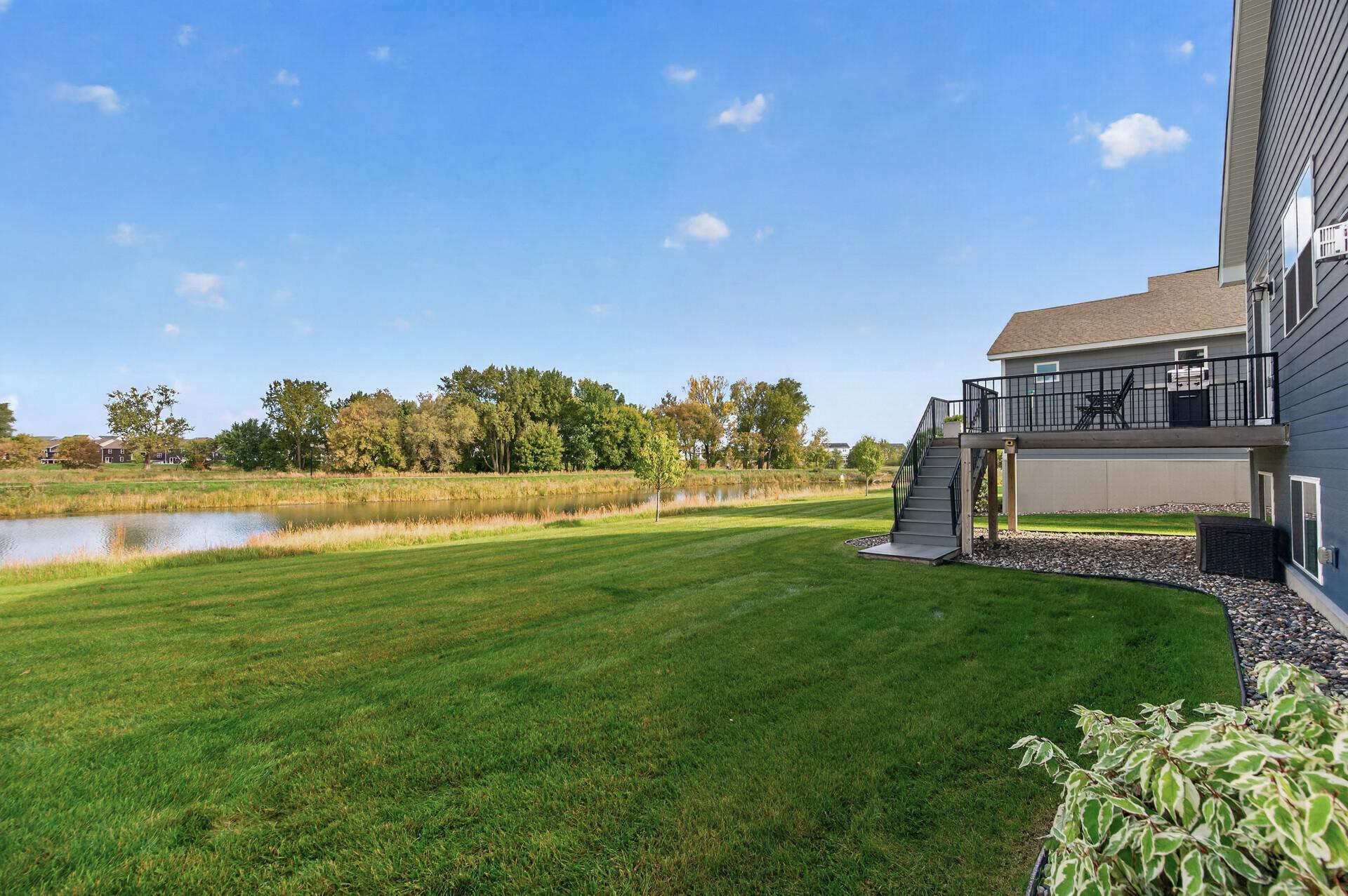Home’s raised deck overlooks a broad lawn and pond bordered by trees.