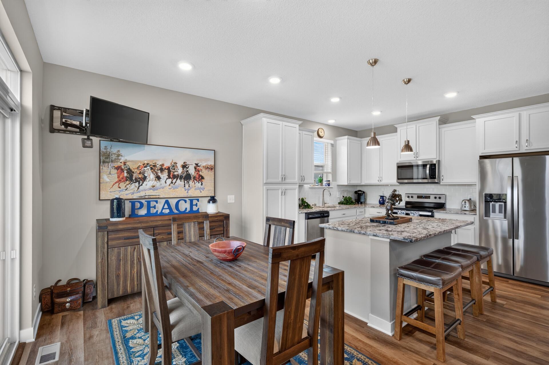 Open kitchen and dining area with white cabinets, granite island, dark wood table, and a blue “PEACE” sign.