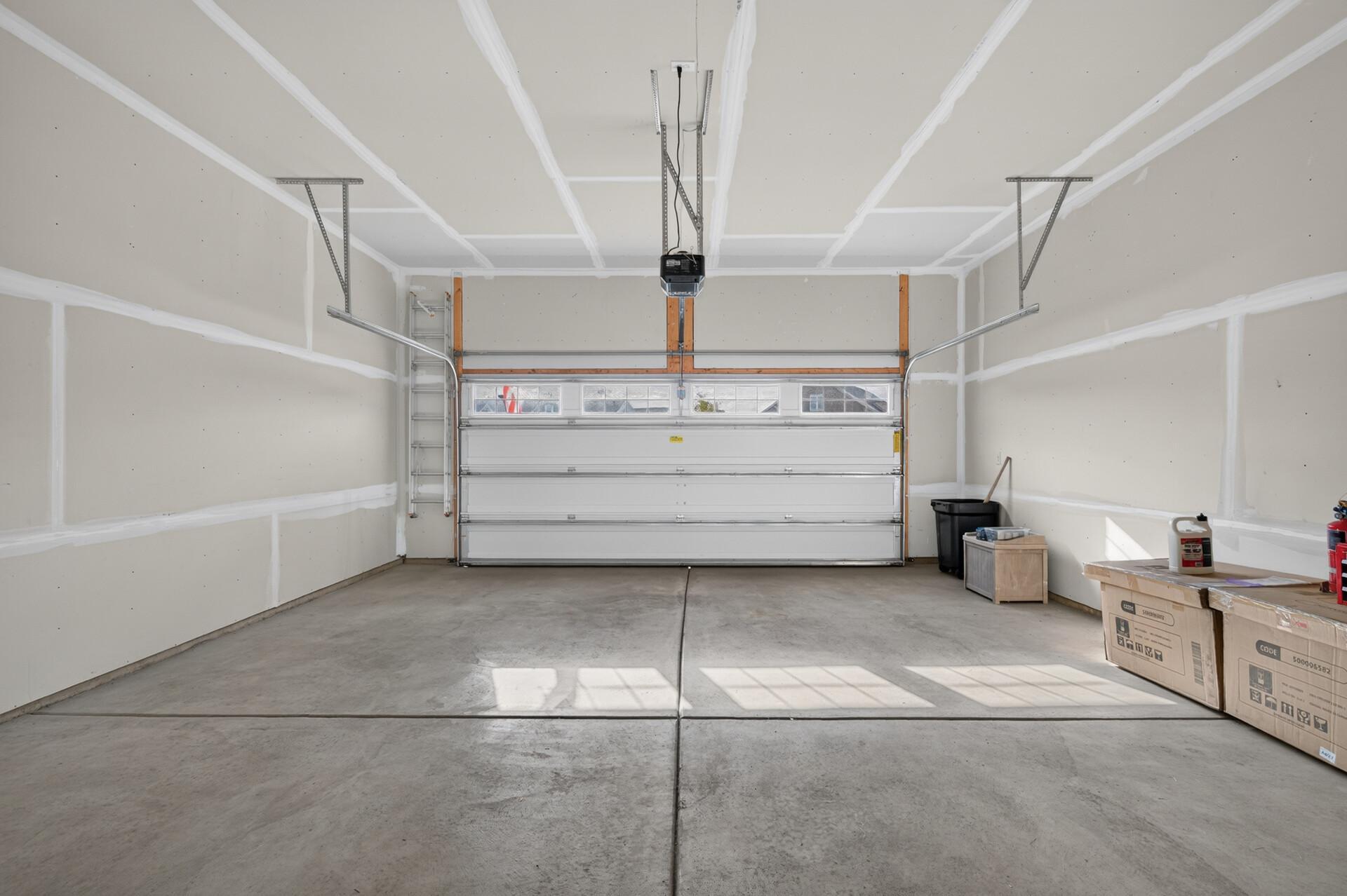 Mostly empty two-car garage with unfinished drywall, concrete floor, and closed overhead door.