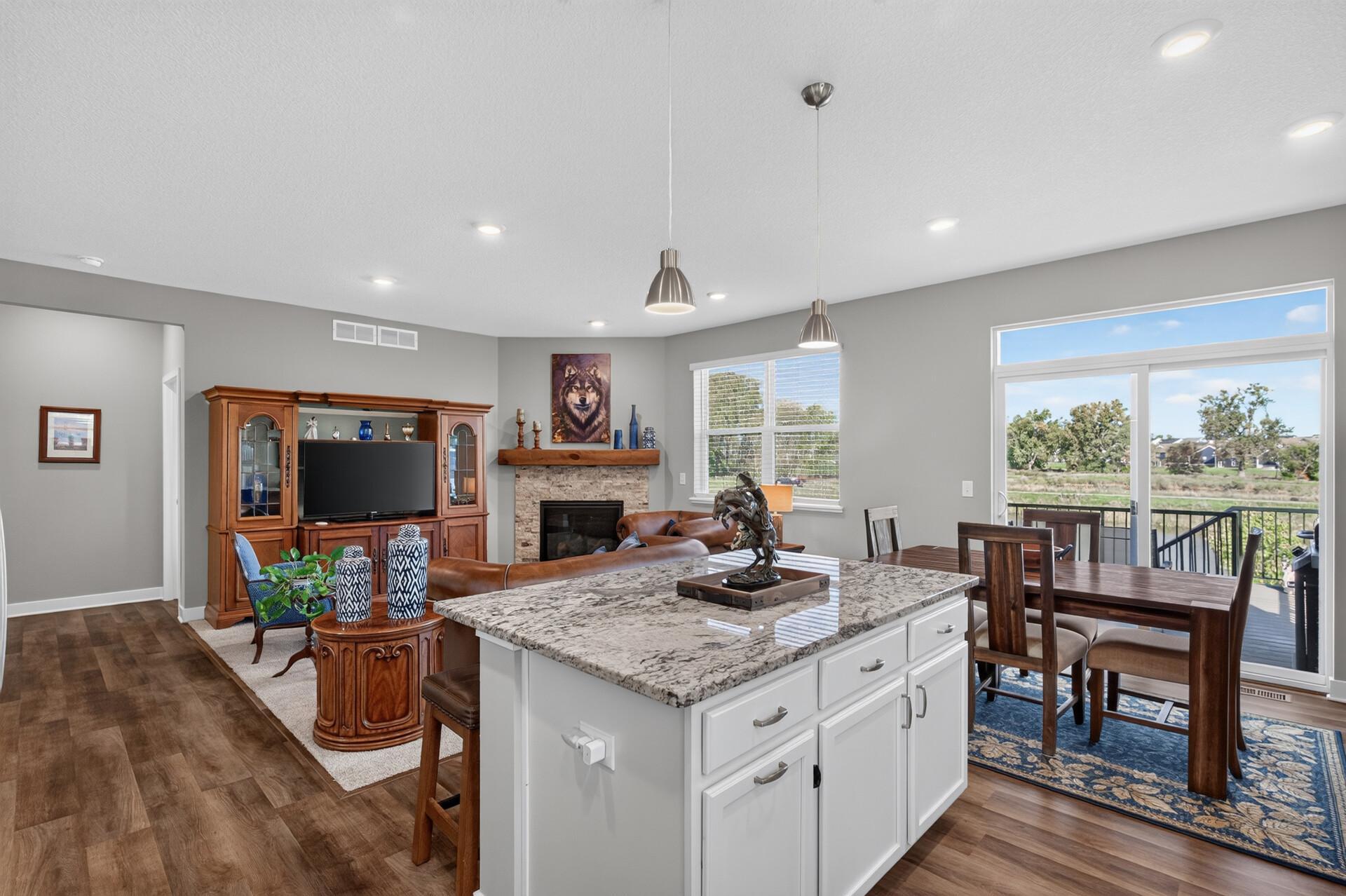 Open-plan kitchen and living room with a large island, stone fireplace, and sliding doors to a deck.