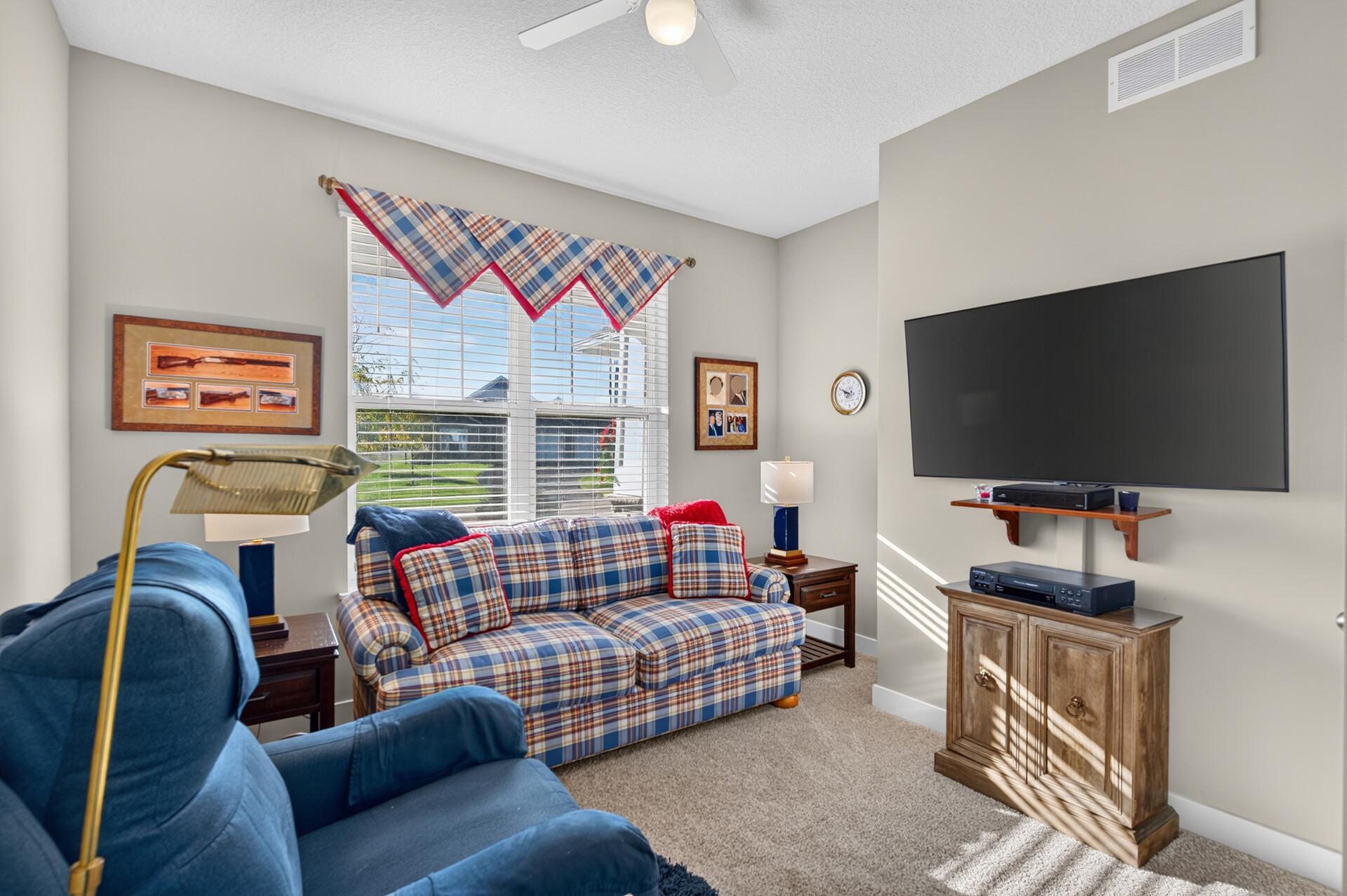 Living room with a plaid sofa, blue armchairs, and a large wall-mounted television.