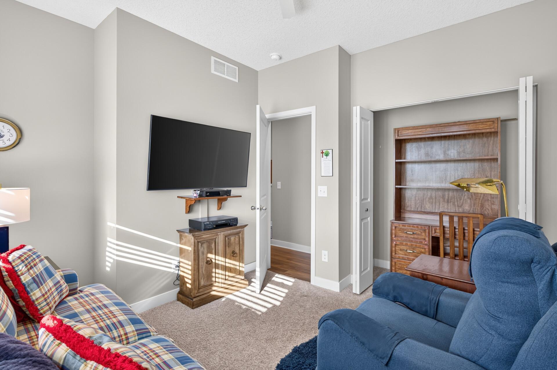 Furnished sitting room with a wall-mounted TV, plaid sofa, blue recliners, and wooden bookcase.