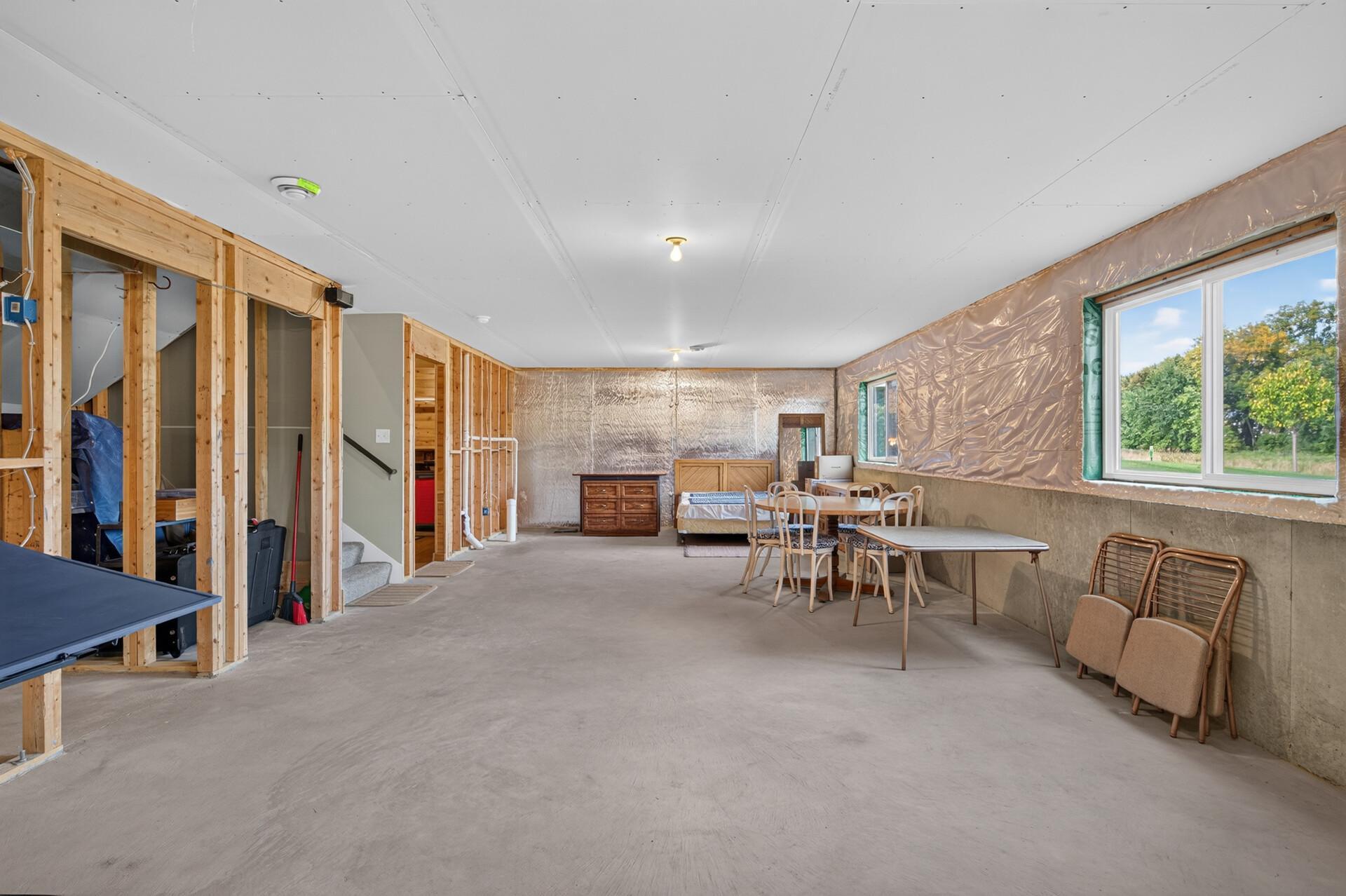 Unfinished basement with exposed framing, concrete floor, and large windows.