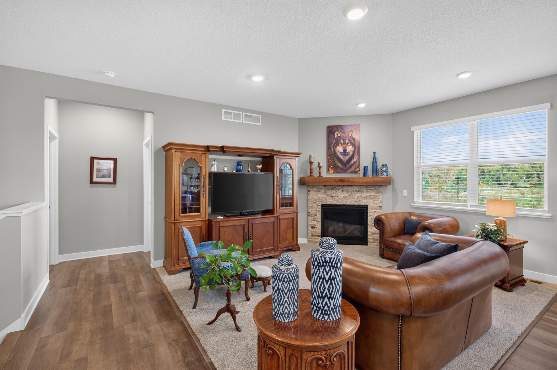 Living room with a stone fireplace, wooden entertainment cabinet, leather seating, and wide windows.