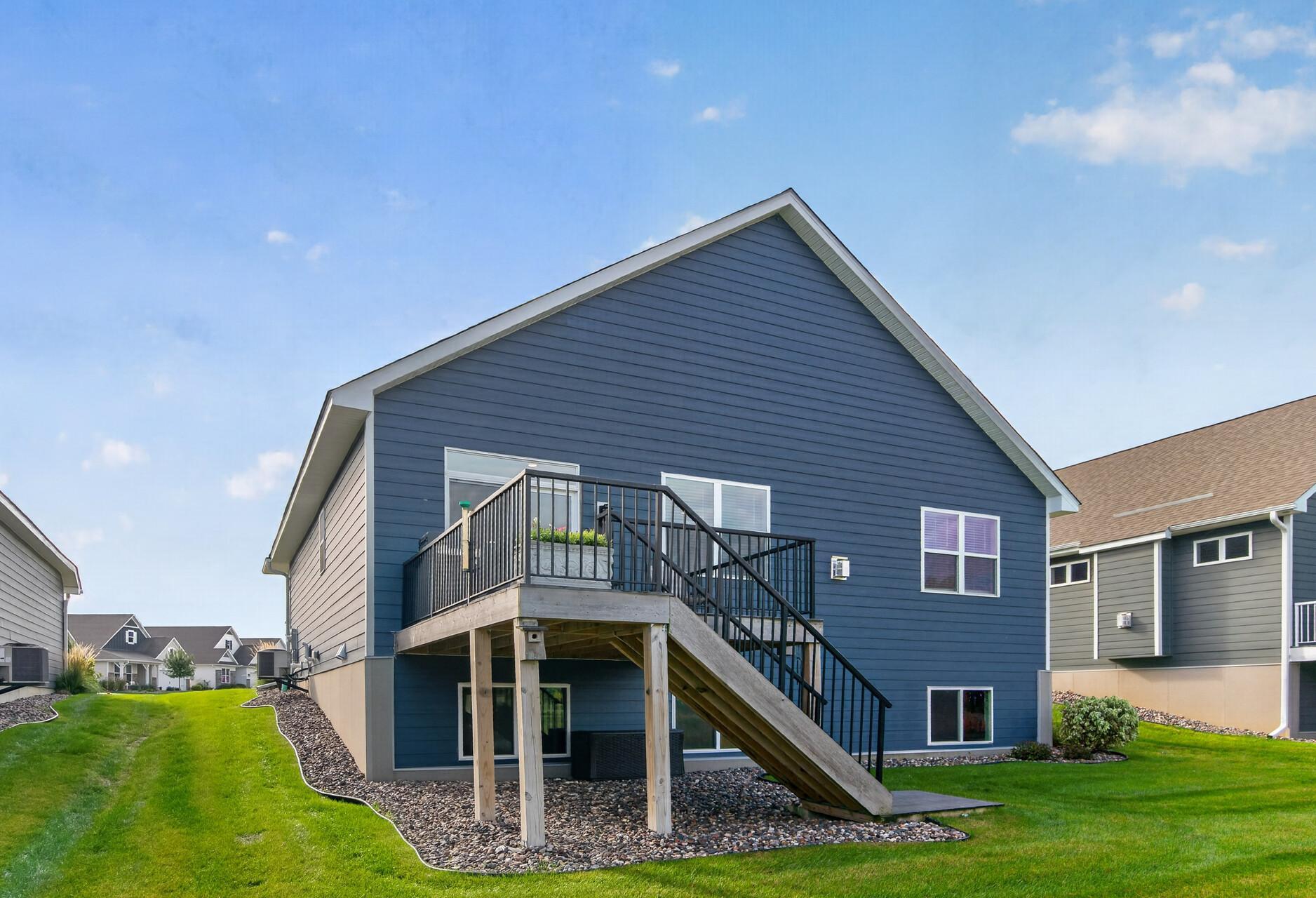 Blue-sided home with a raised deck and stairs overlooking a green lawn.